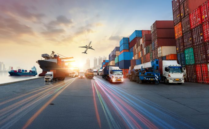 Containerterminal met vrachtwagens en schepen bij zonsondergang.