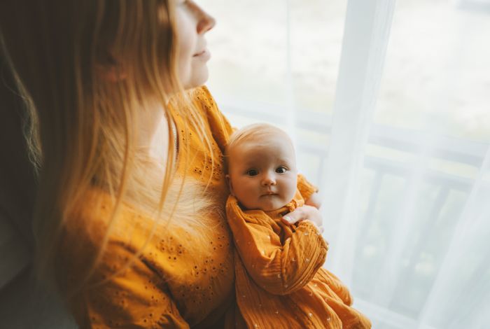 Ouder houdt een baby vast bij een raam.