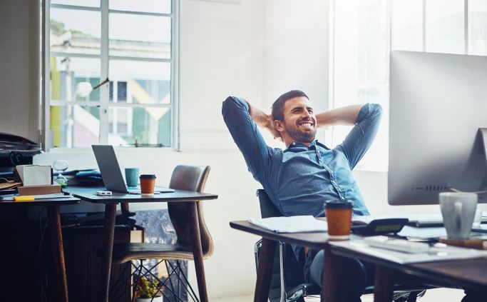 Medewerker leunt ontspannen achterover aan zijn bureau.