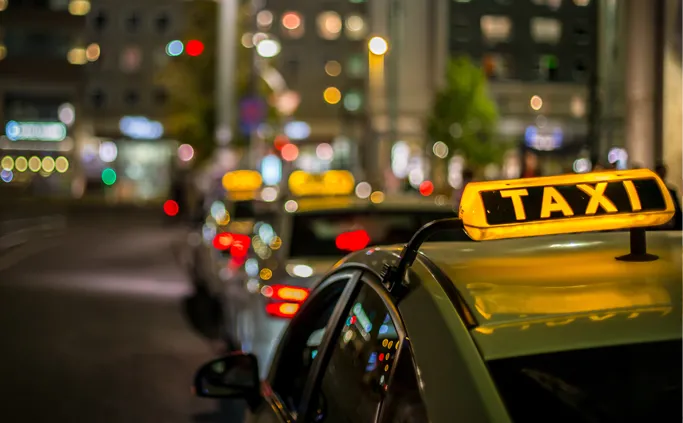 Taxi met een verlicht dakbord in een drukke straat bij nacht.